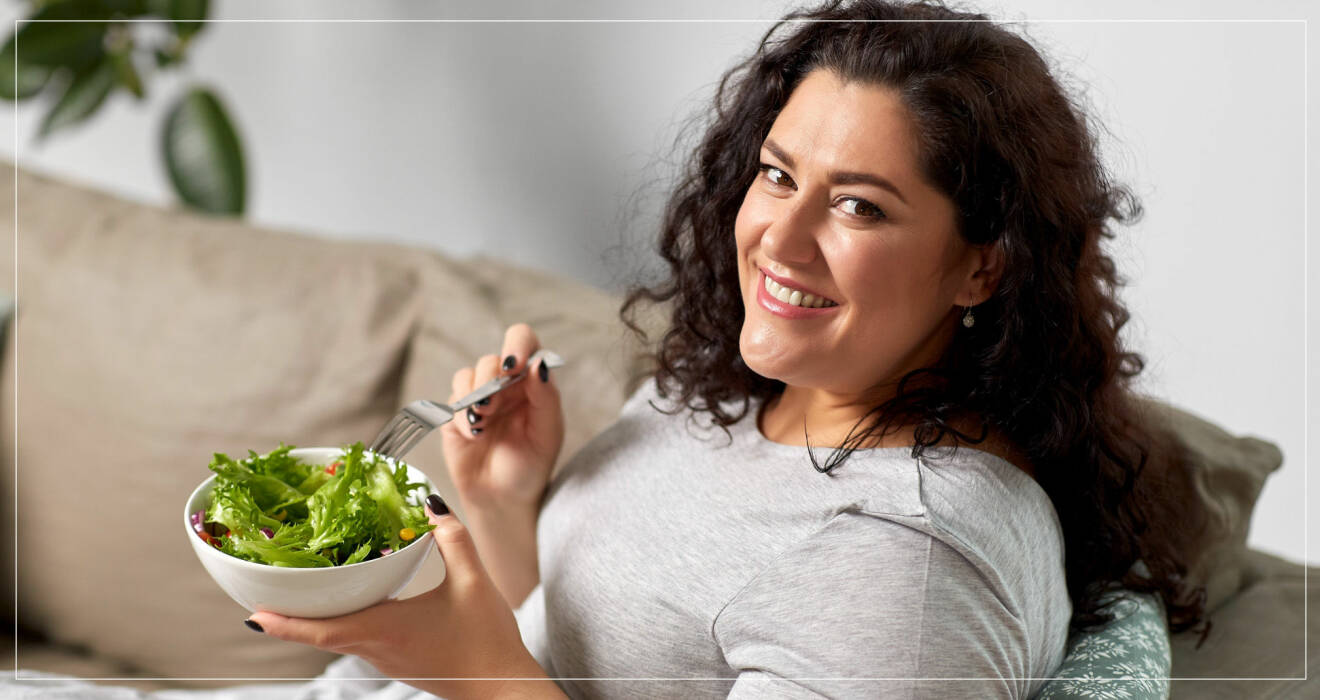 Kurvig kvinna äter sallad i soffa.