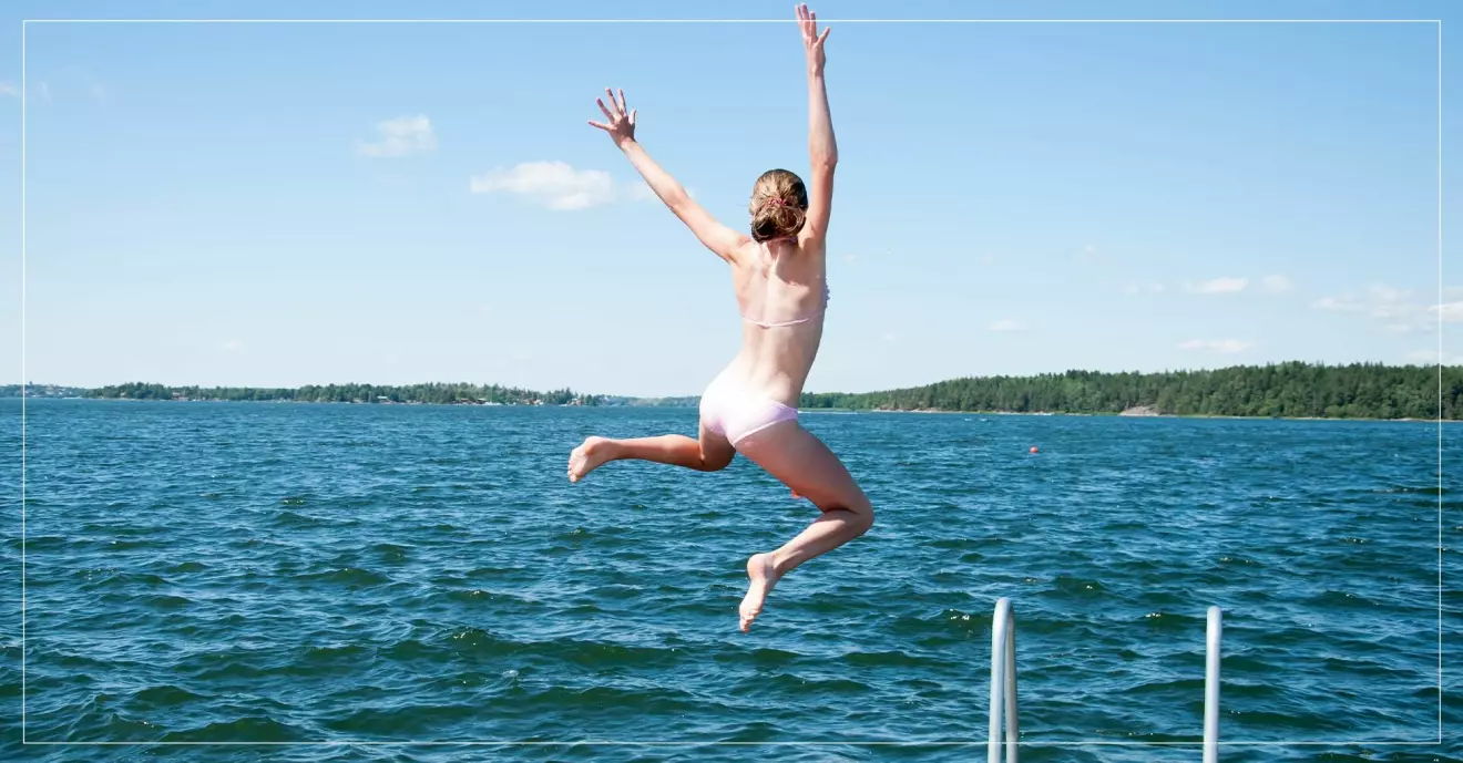 Kvinna badar och hoppar glatt ifrån brygga ned i vattnet.