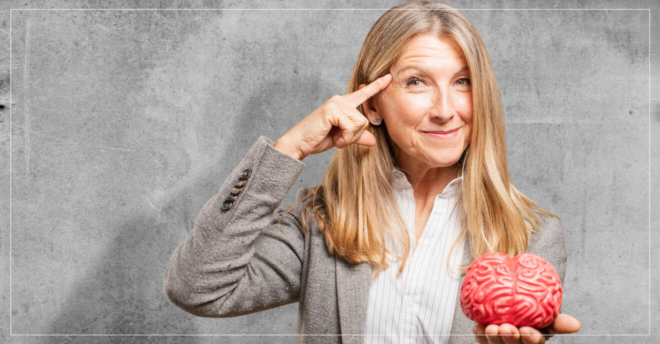 Äldre kvinna som håller i en konstgjord hjärna och pekar på sitt huvud.