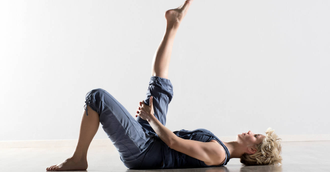 Kvinna som ligger på golvet och stretchar baksida lår genom att sträcka på benet.