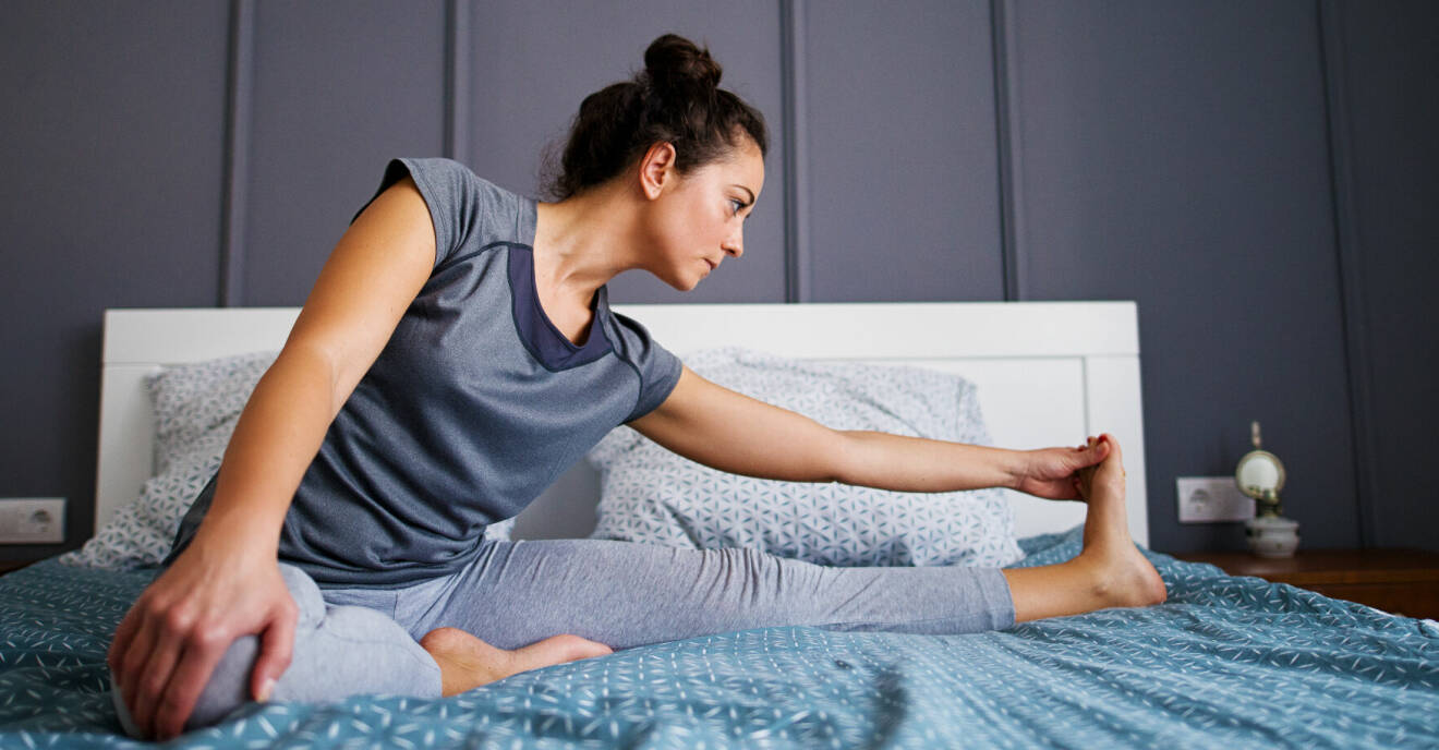Kvinna stretchar i sängen på morgonen för att det hjälper mot stela knän
