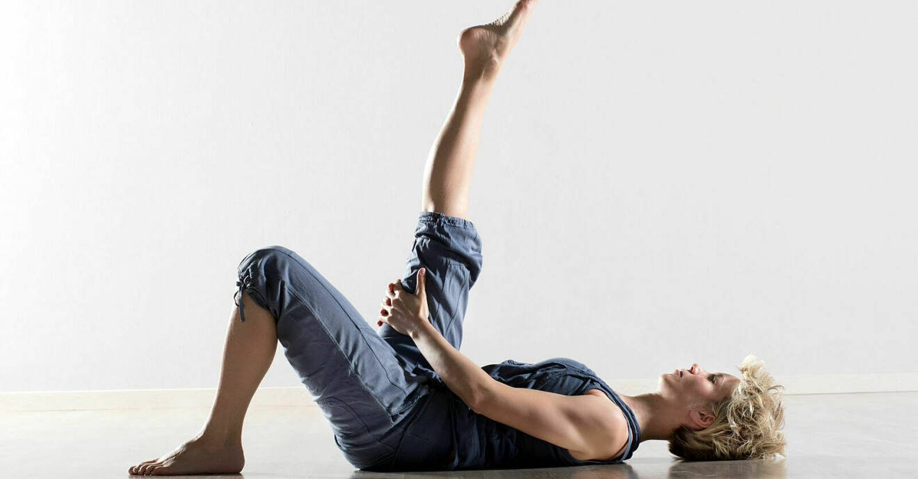 Kvinna som stretchar baksida lår liggandes på golvet.