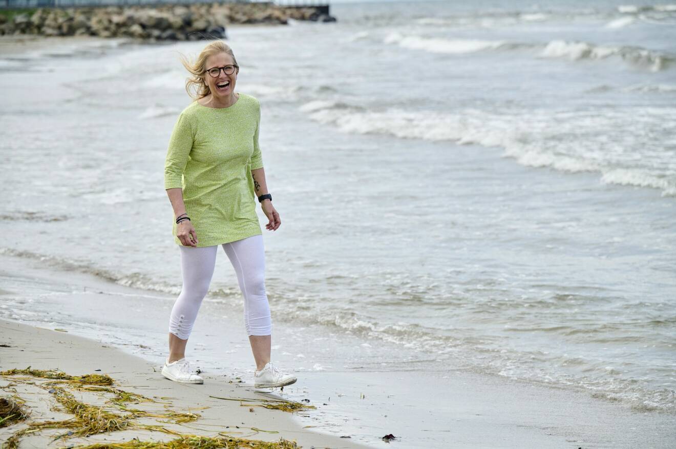 En medelålders kvinna går längs havet och skrattar.