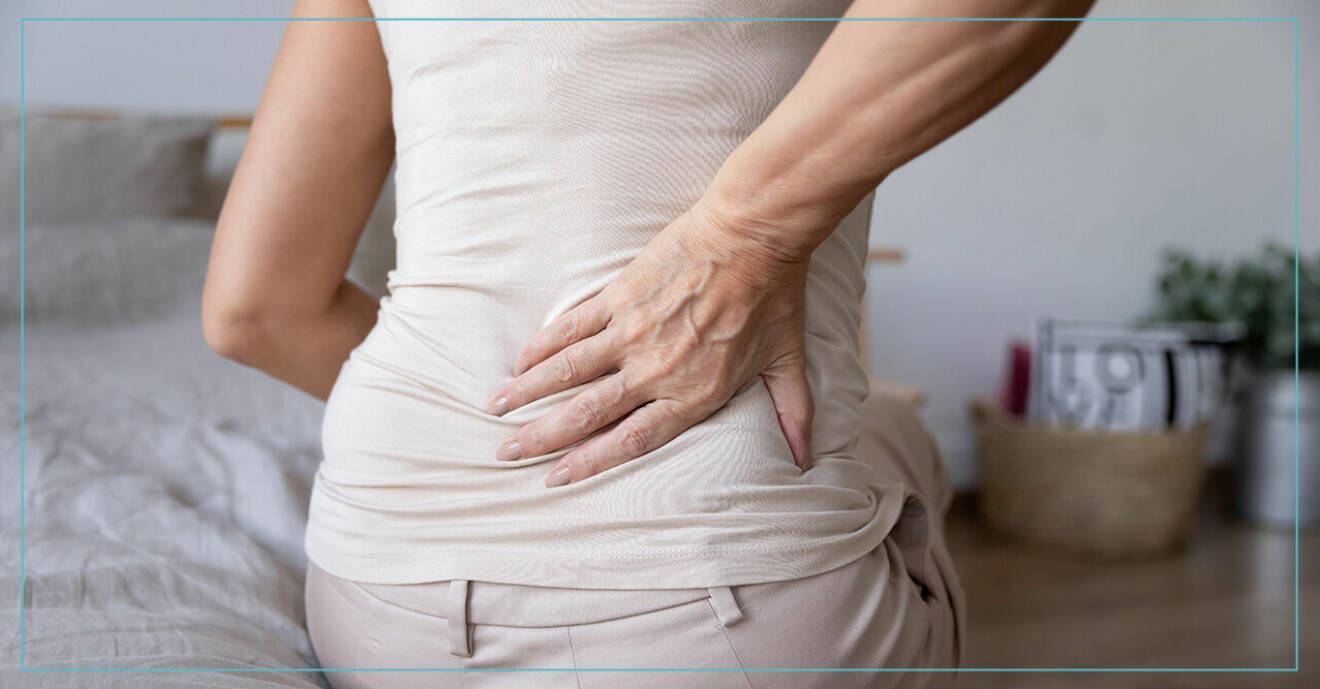 Kvinna som håller sig för höger sida av ryggen på grund av smärta.