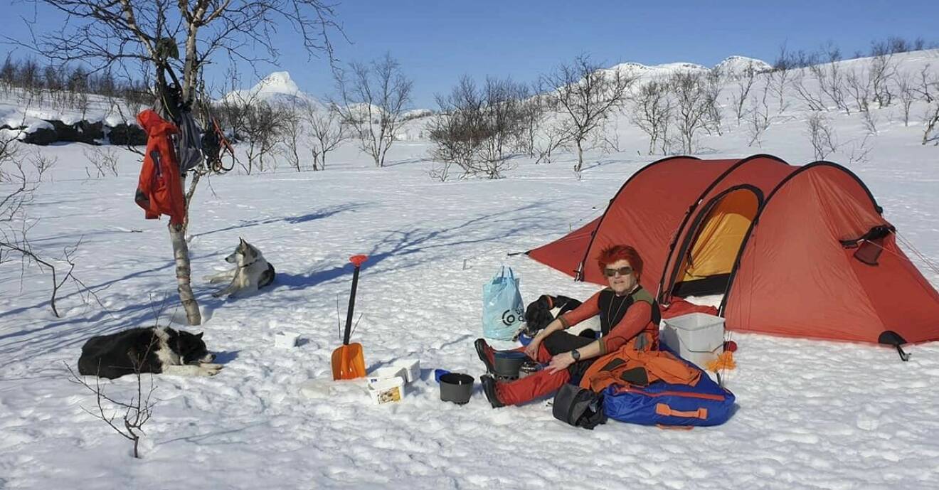Birgitta sitter på snön utanför sitt tält.