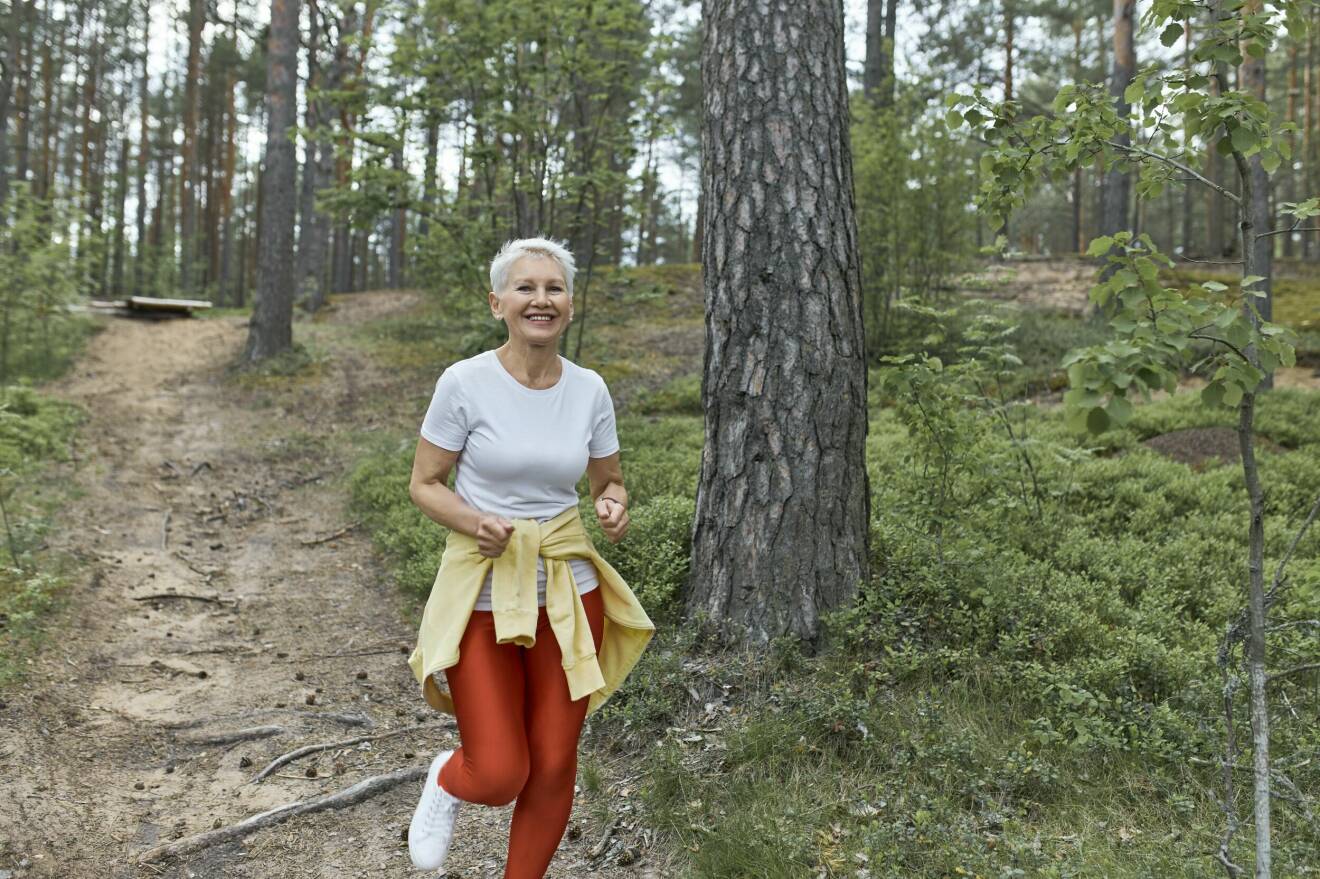 kvinna joggar med ett leende i skogen