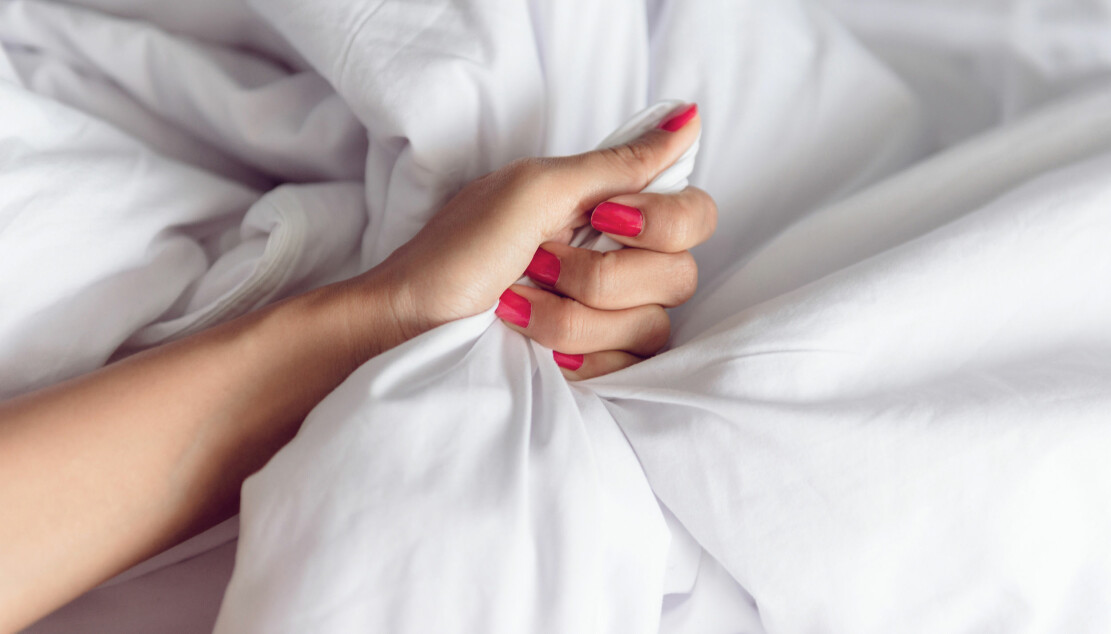 Kvinna i säng kramar lakan medan hon får orgasm.
