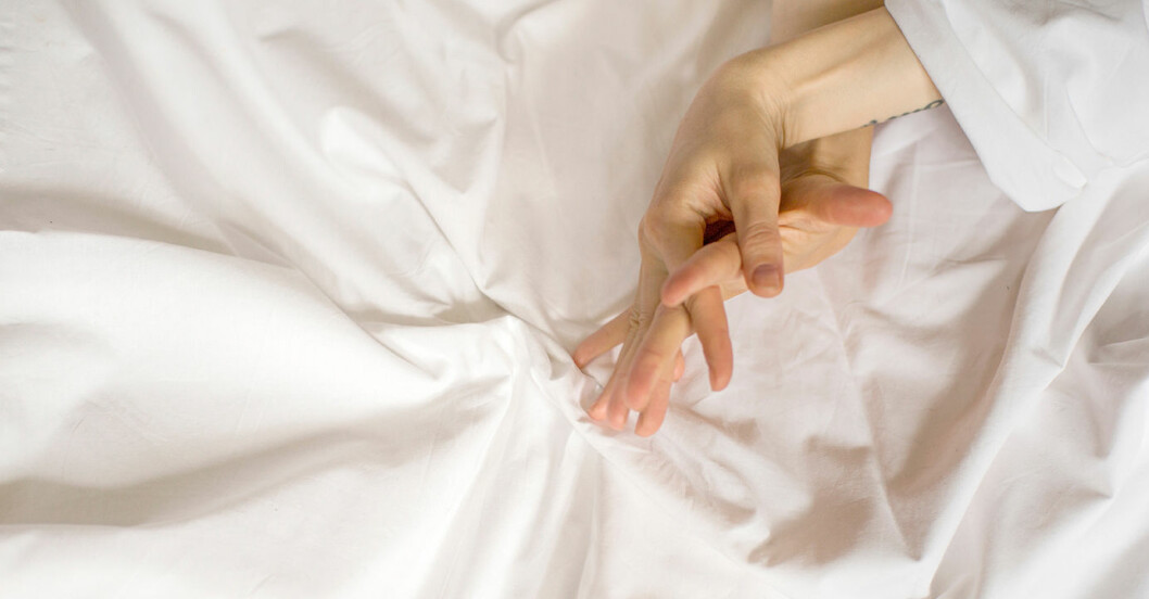 En man och en kvinna håller hand när de får orgasm i en säng med vita lakan.