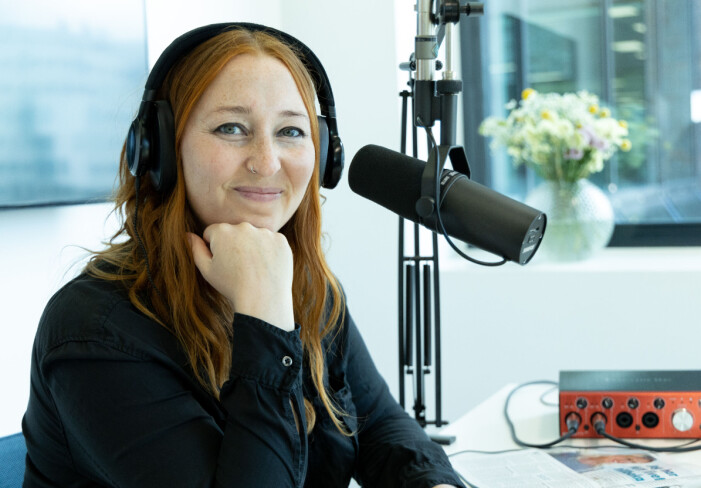 Elin Samuelsson är programledare för den nya podcasten <em>Lätta ditt hjärta</em>, som spelas in i Malmö. Porträttbild på Elin Samuelsson som sitter i en poddstudio med hörlurar på öronen och en stor mikrofon framför sig.