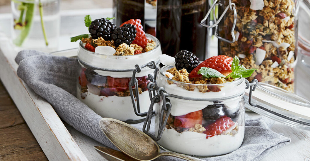 Två glasburkar med yoghurt, jordgubbar, björnbär och granola på fin dukning