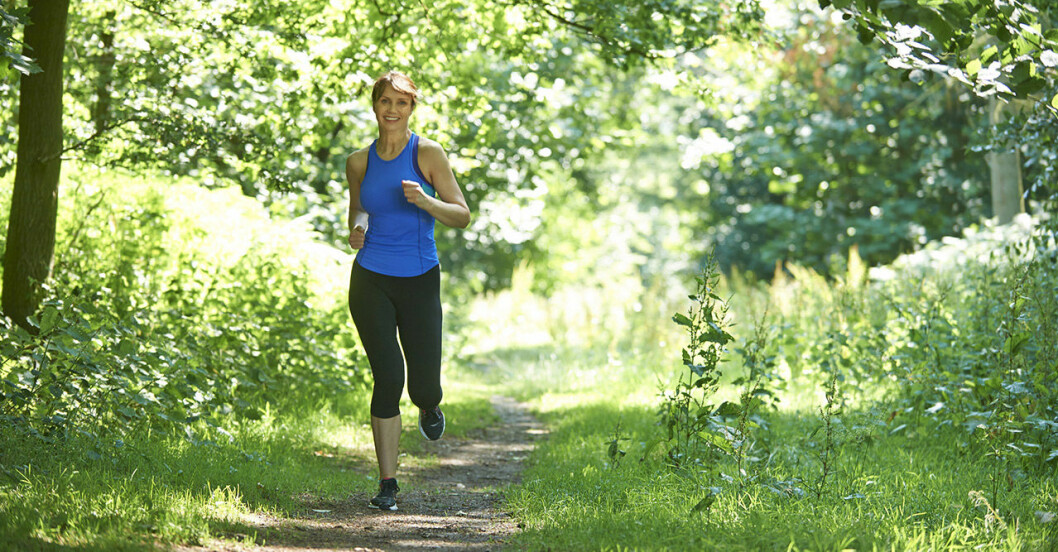 Glad kvinna joggar i skogen.