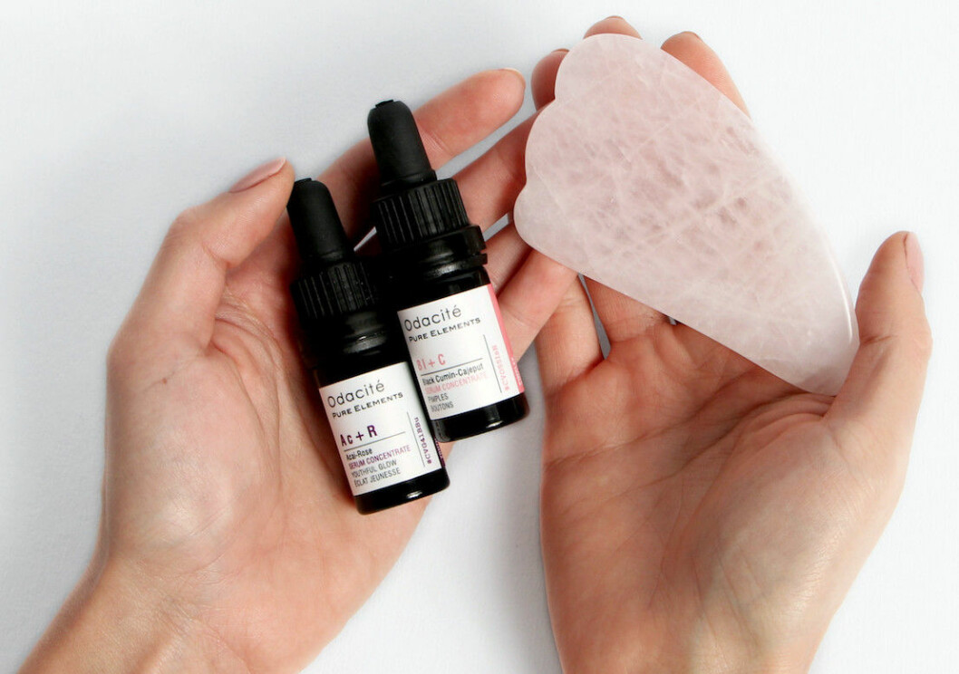 Två händer som håller i serum och rosa gua sha-sten