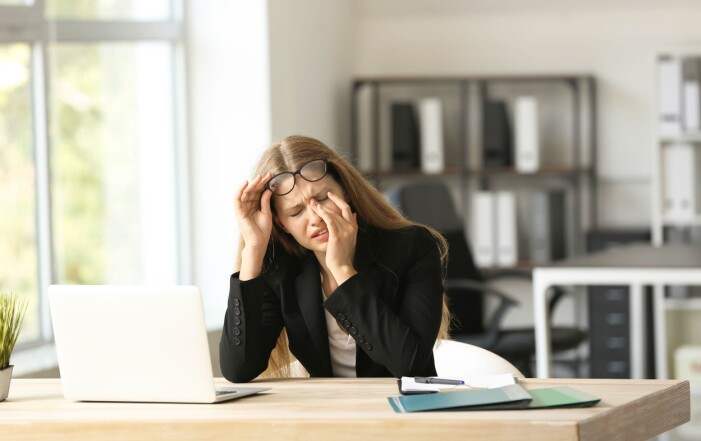 Problem med stress måste man ta tag i. Kvinna vid dator med huvudvärk.