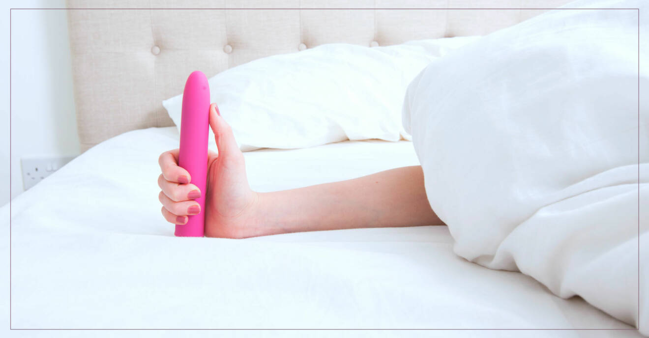 Kvinnas arm stickar fram under täcker och i handen håller hon en rosa dildo.