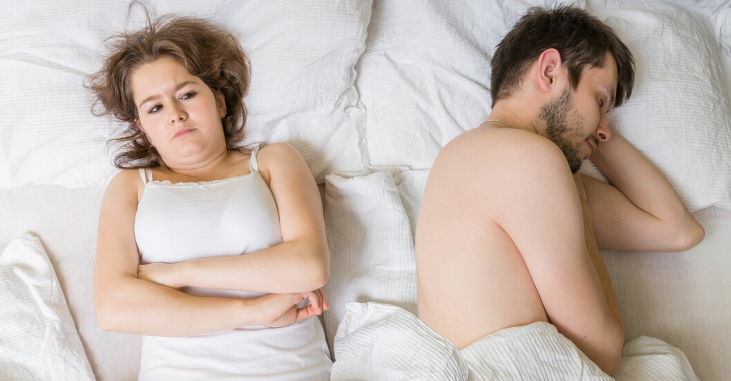 Kvinna med missnöjt ansiktsuttryck ligger bredvid sovande man i en säng