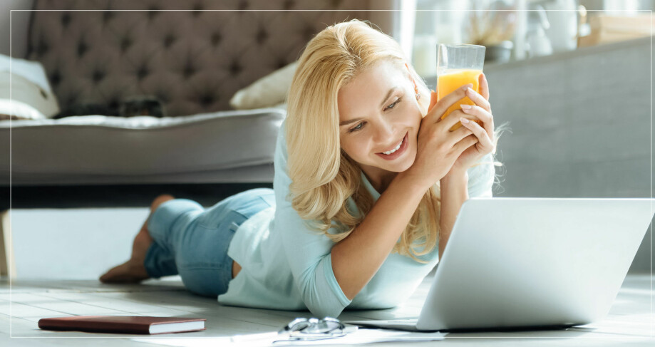 kvinna dricker juice framför datorn.