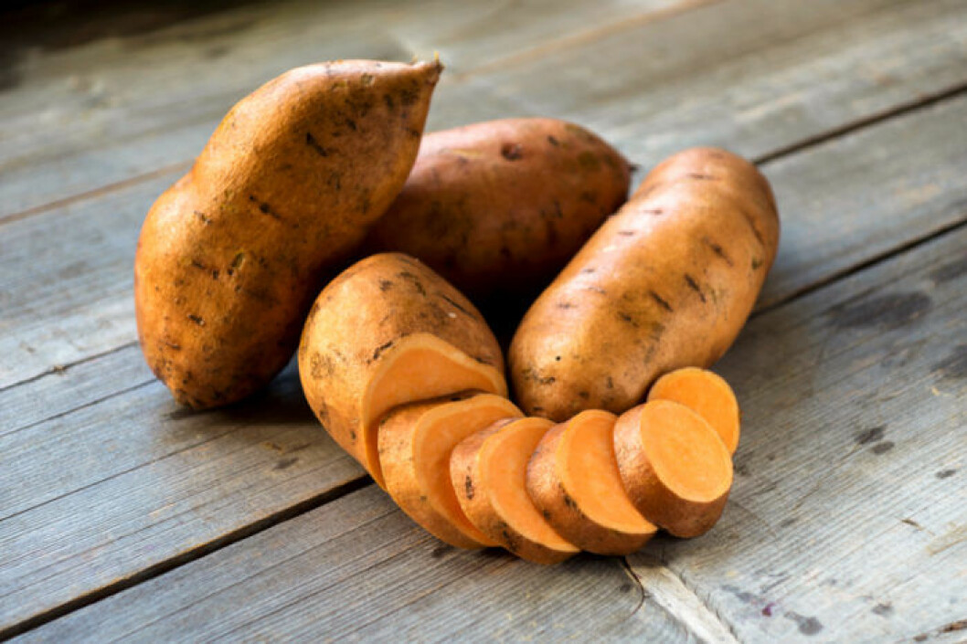 Hel och skivad rå sötpotatis på trägolv.