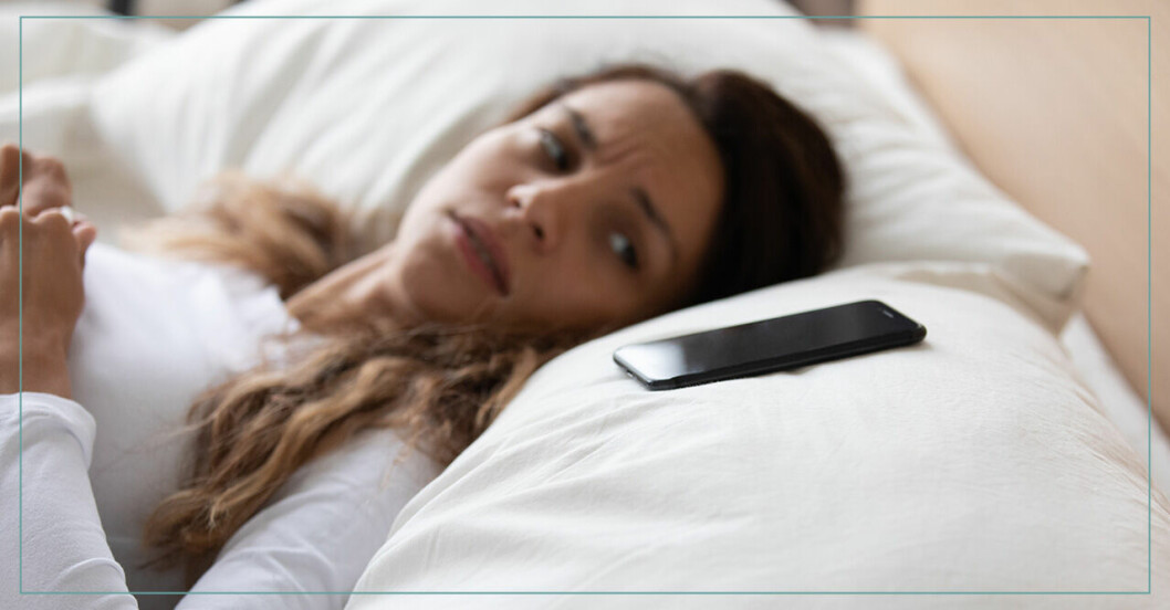 Orolig kvinna ligger i sängen bredvid sin mobiltelefon