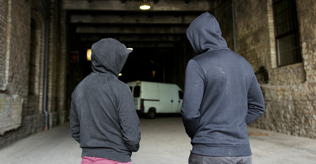 Två unga killar i hoddies står i mörk gång med en skåpbil som skymtar i bakgkrunden.