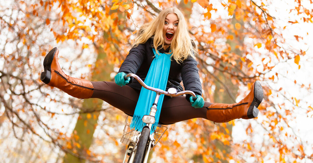 Ung kvinna cyklar i höstskog, skrattar och släpper taget om pedalerna.