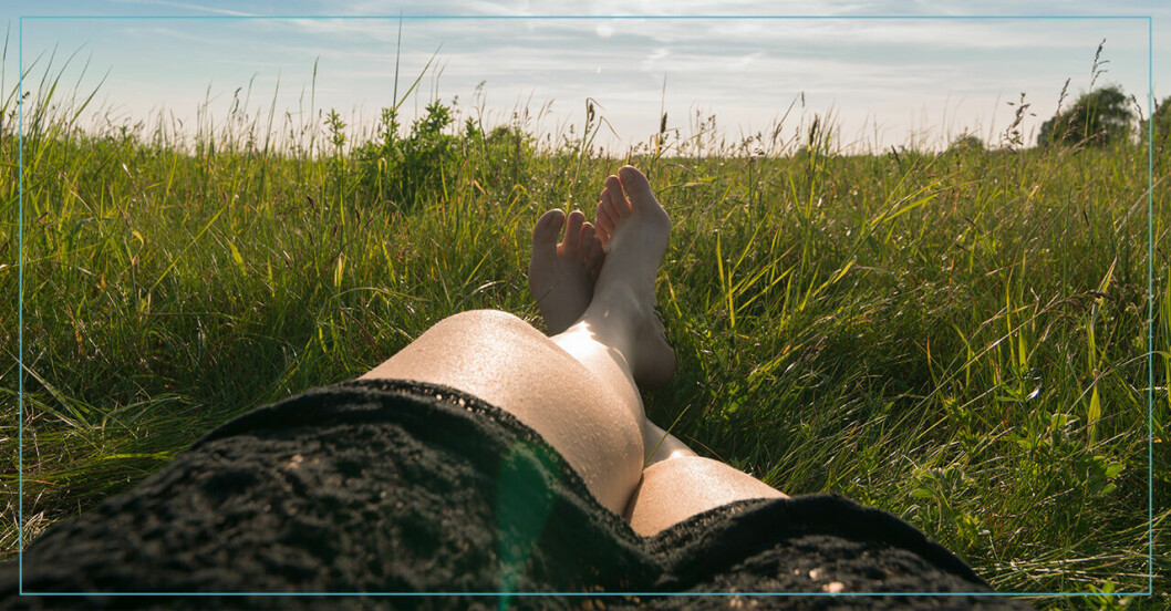 Kvinna ligger med bara ben i solsken i gräset